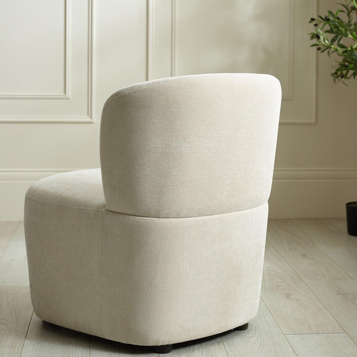 Beige upholstered accent chair with curved backrest on light wood floor near wall paneling
