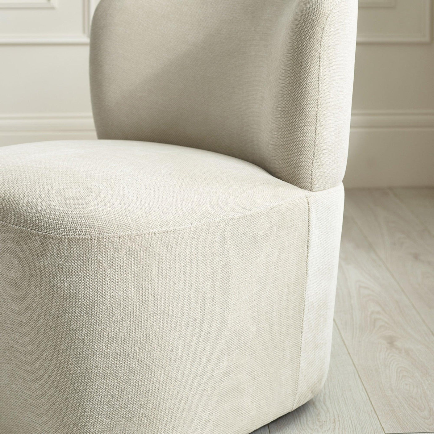 Beige fabric accent chair with curved back on light wood flooring