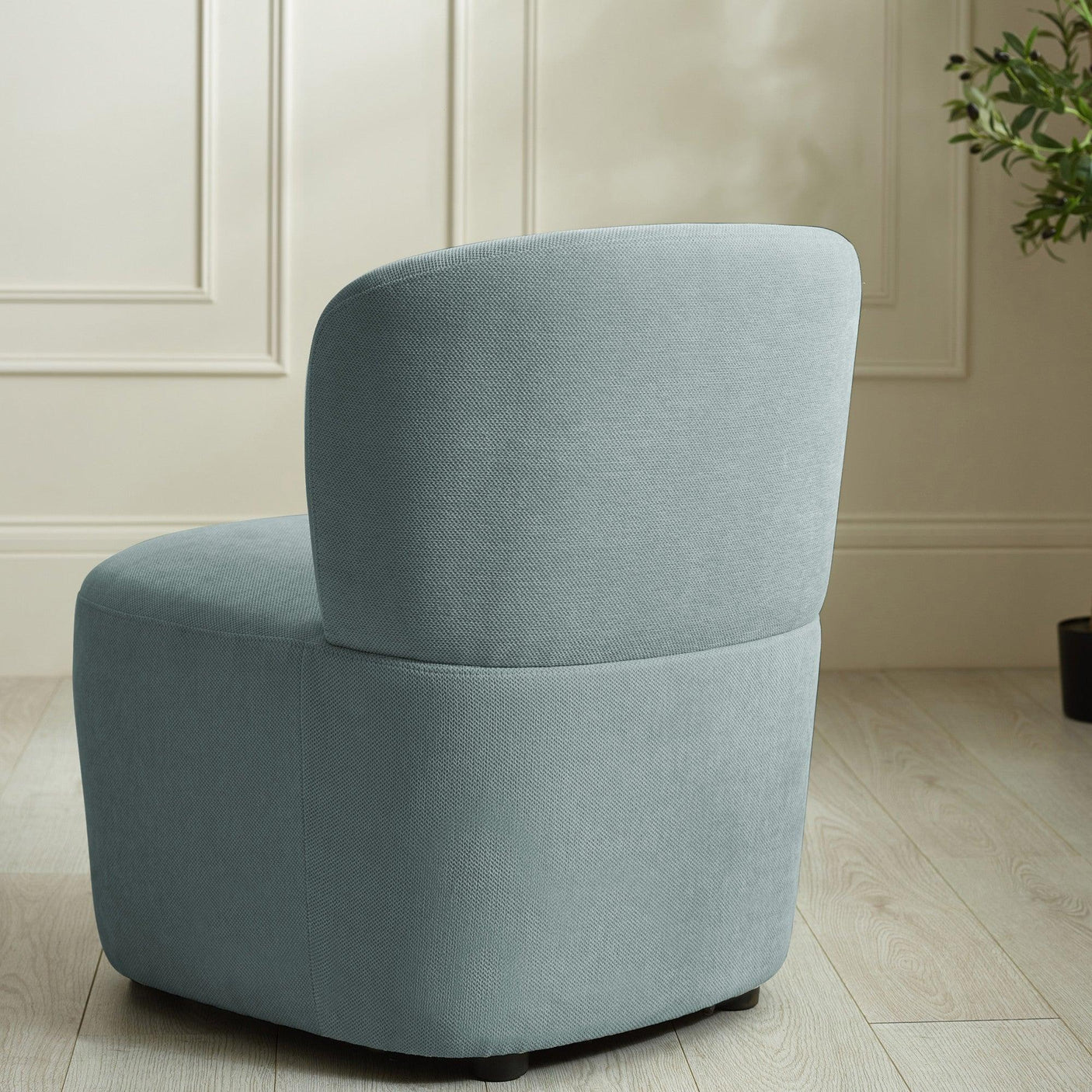 Light blue accent chair with curved backrest on wood floor beside cream wall paneling
