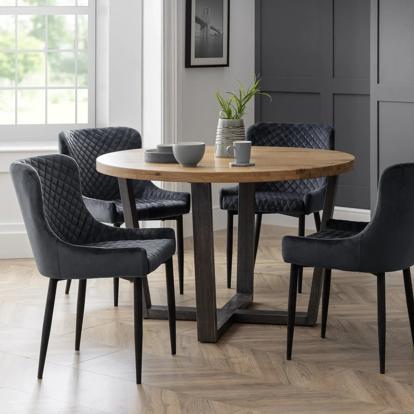 Grey velvet dining chairs with diamond stitching around wooden round dining table in modern room