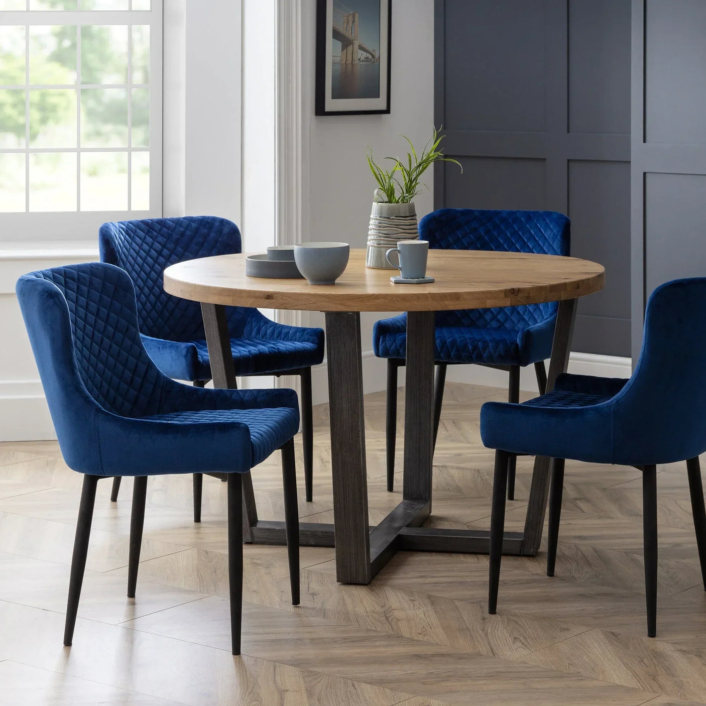 Blue velvet dining chairs with quilted backs around round wooden table in modern dining room
