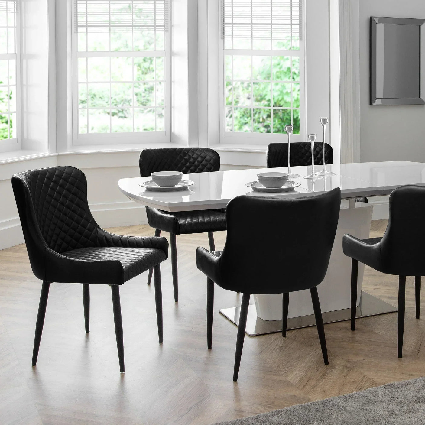 Black faux leather dining chairs around a white table in a modern dining room