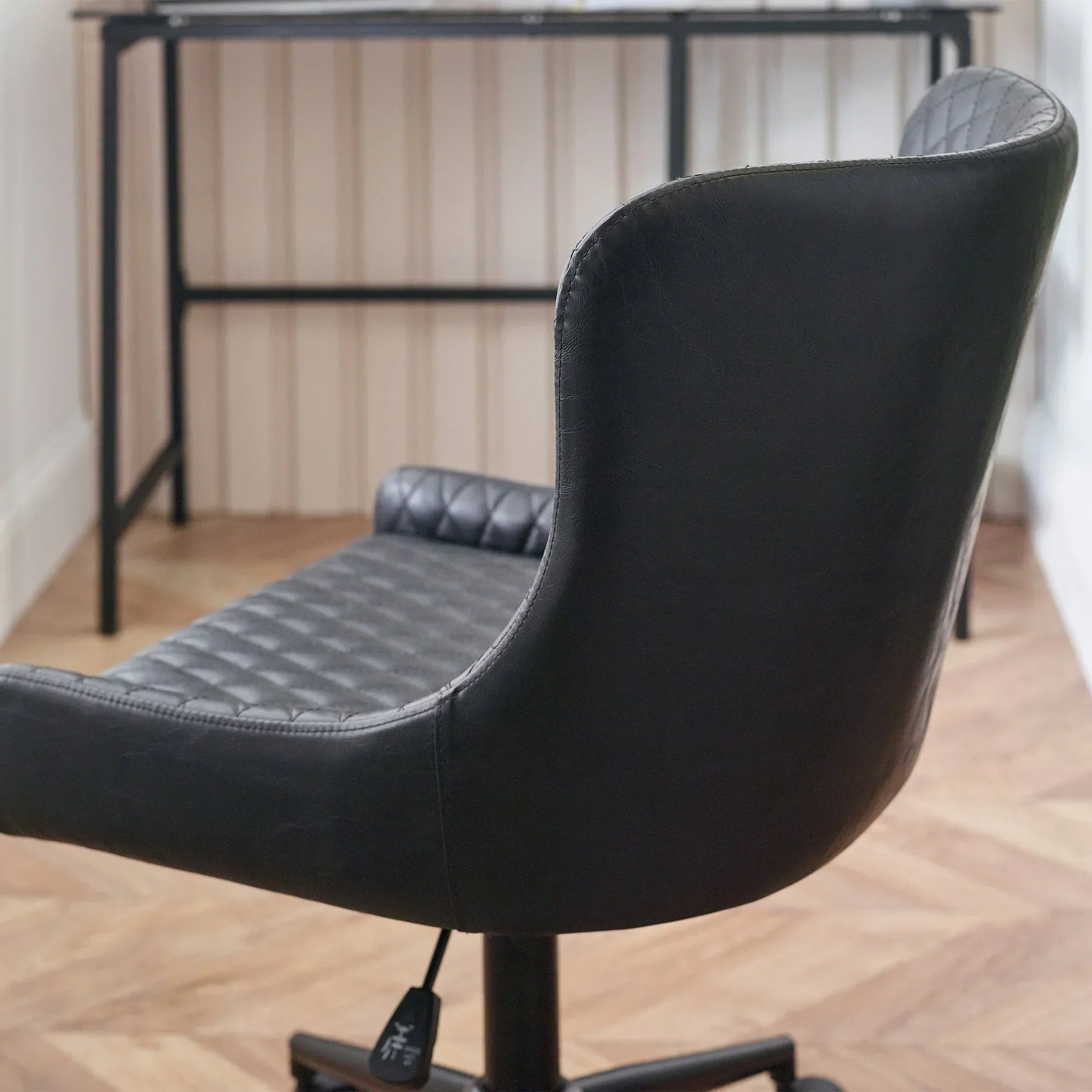 Black faux leather office chair with quilted seat and backrest in front of desk