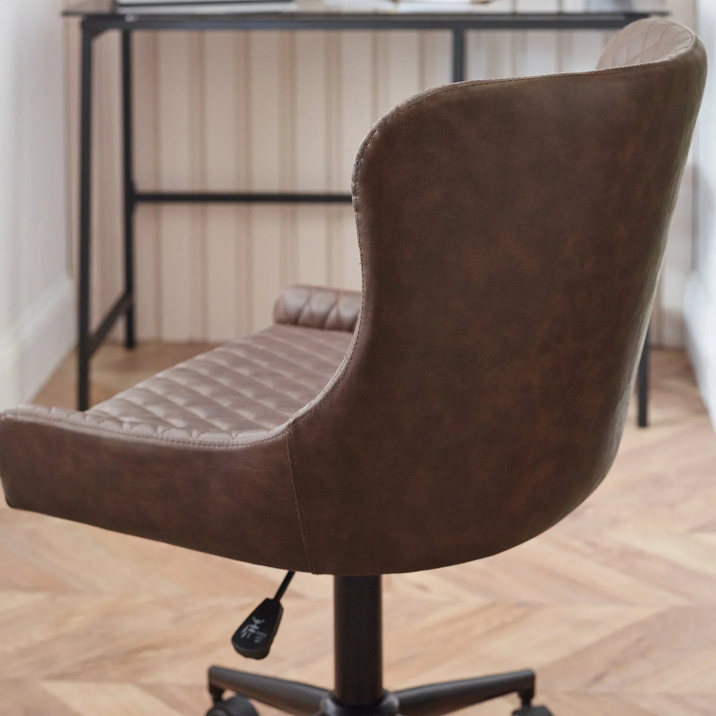 Brown faux leather office chair with quilted seat and curved backrest, side angle view