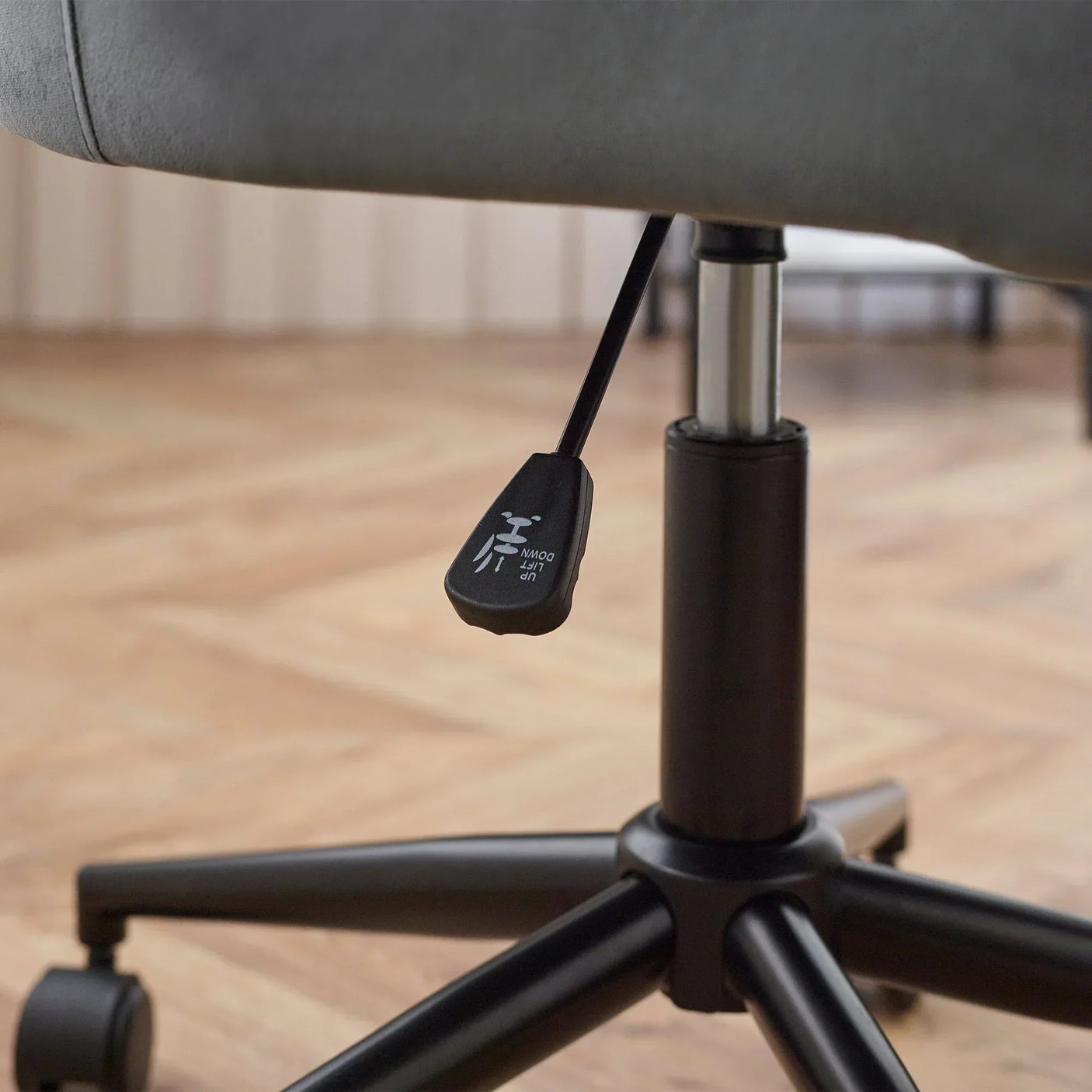 Grey velvet office chair height adjustment lever and black swivel base close up