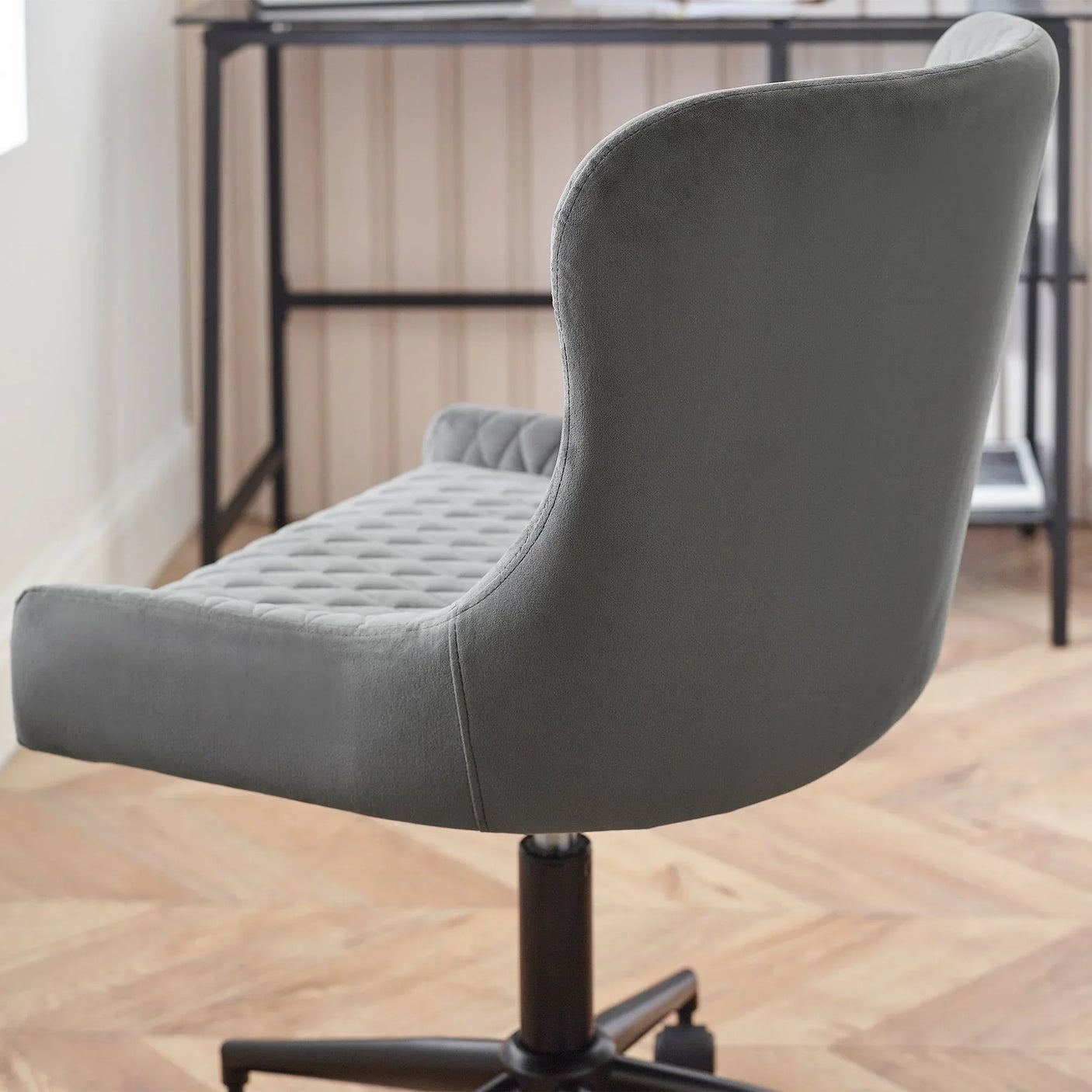 Grey velvet office chair with quilted seat and curved backrest on wood floor