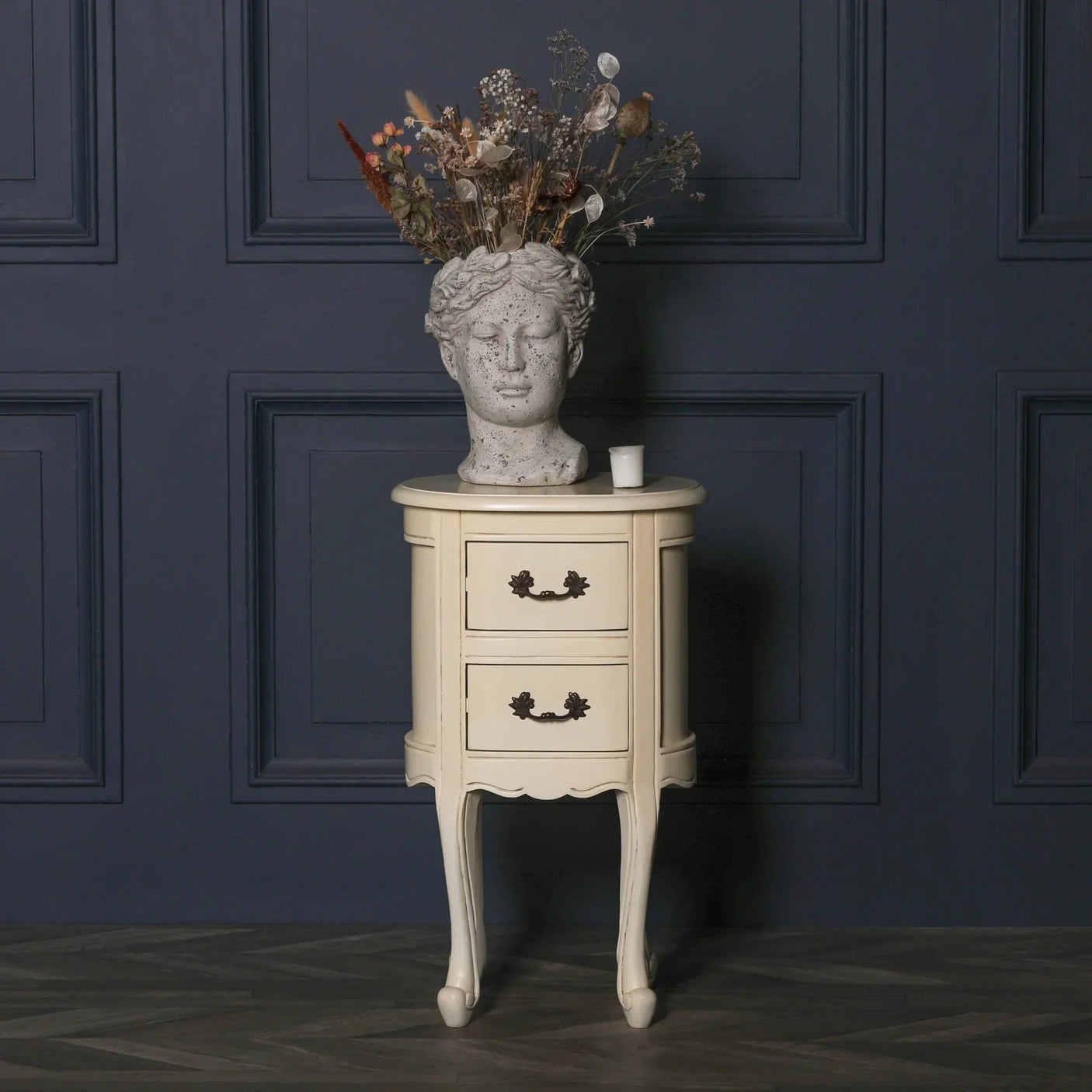 Cream bedside table with two drawers against dark blue wall, statue vase on top