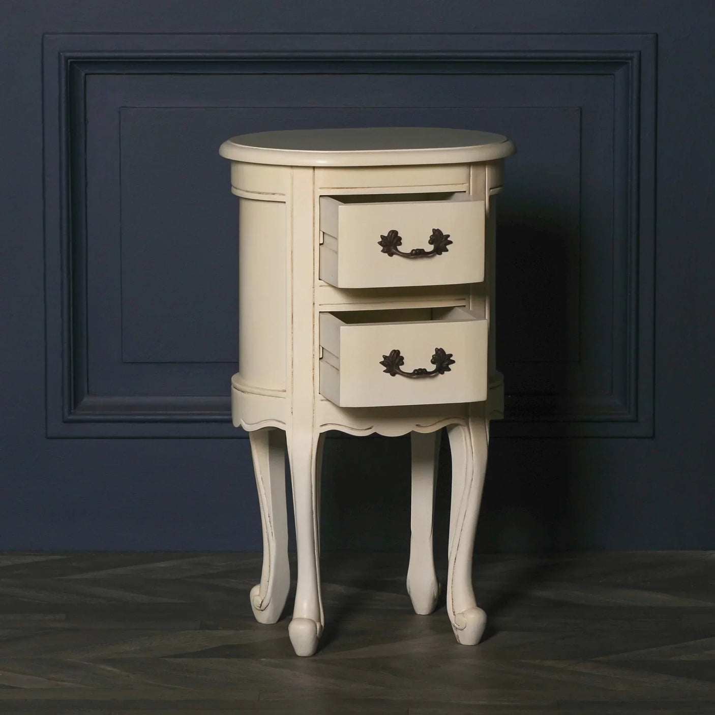 Cream bedside table with two open drawers and curved legs against dark wall