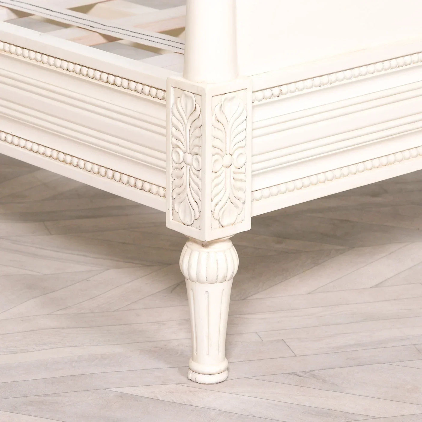 Close view of carved wooden bed frame corner in painted ivory finish with fluted leg
