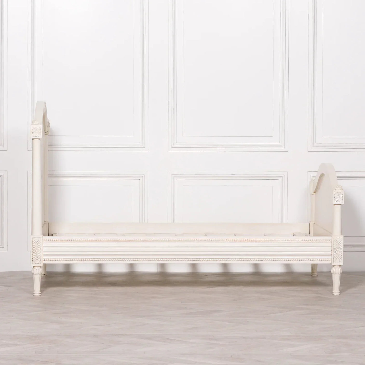 Cream wooden day bed with carved details and high scrolled ends against white panelled wall