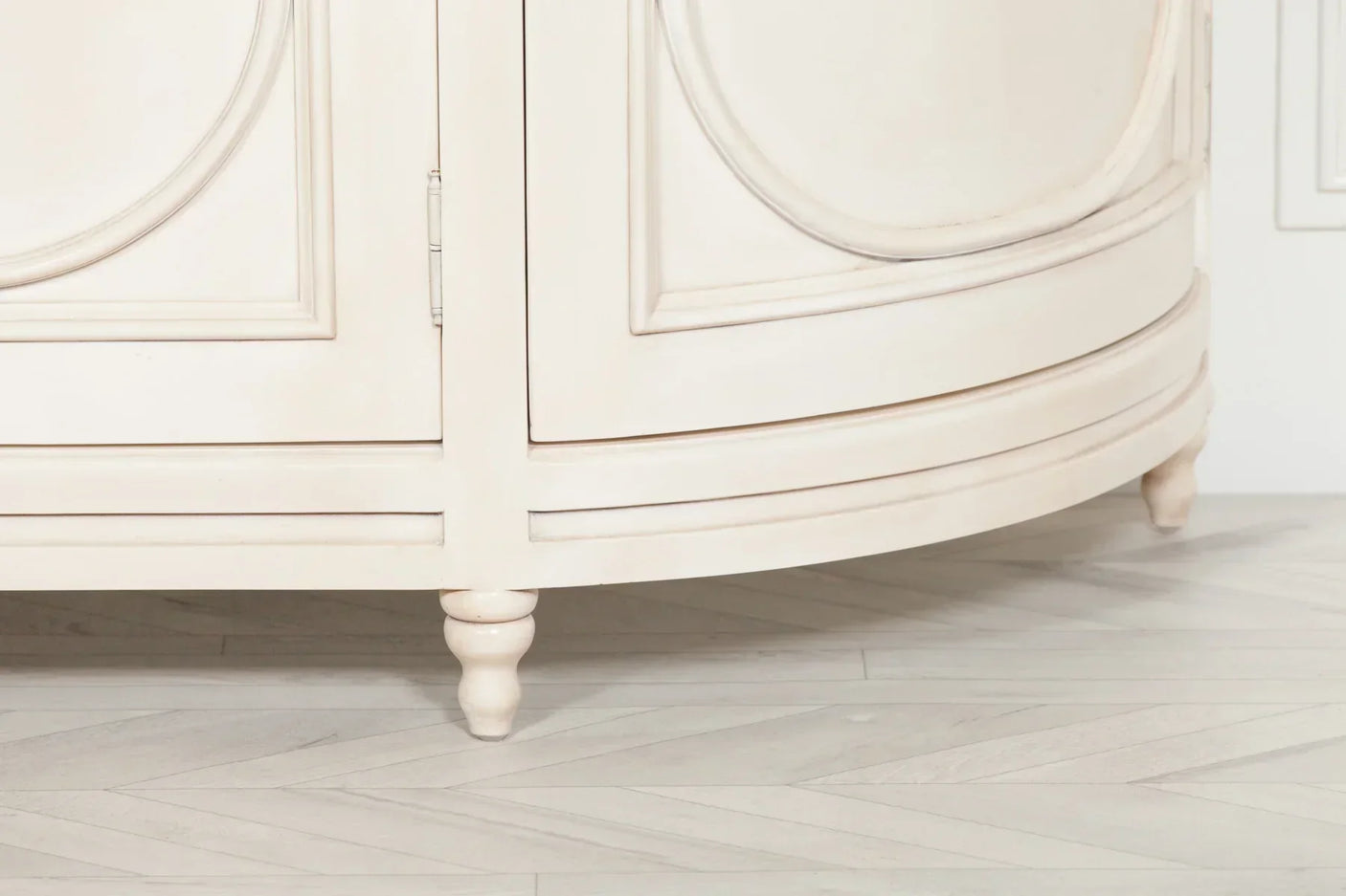 Cream painted wooden sideboard with panel detail and turned legs on light herringbone floor