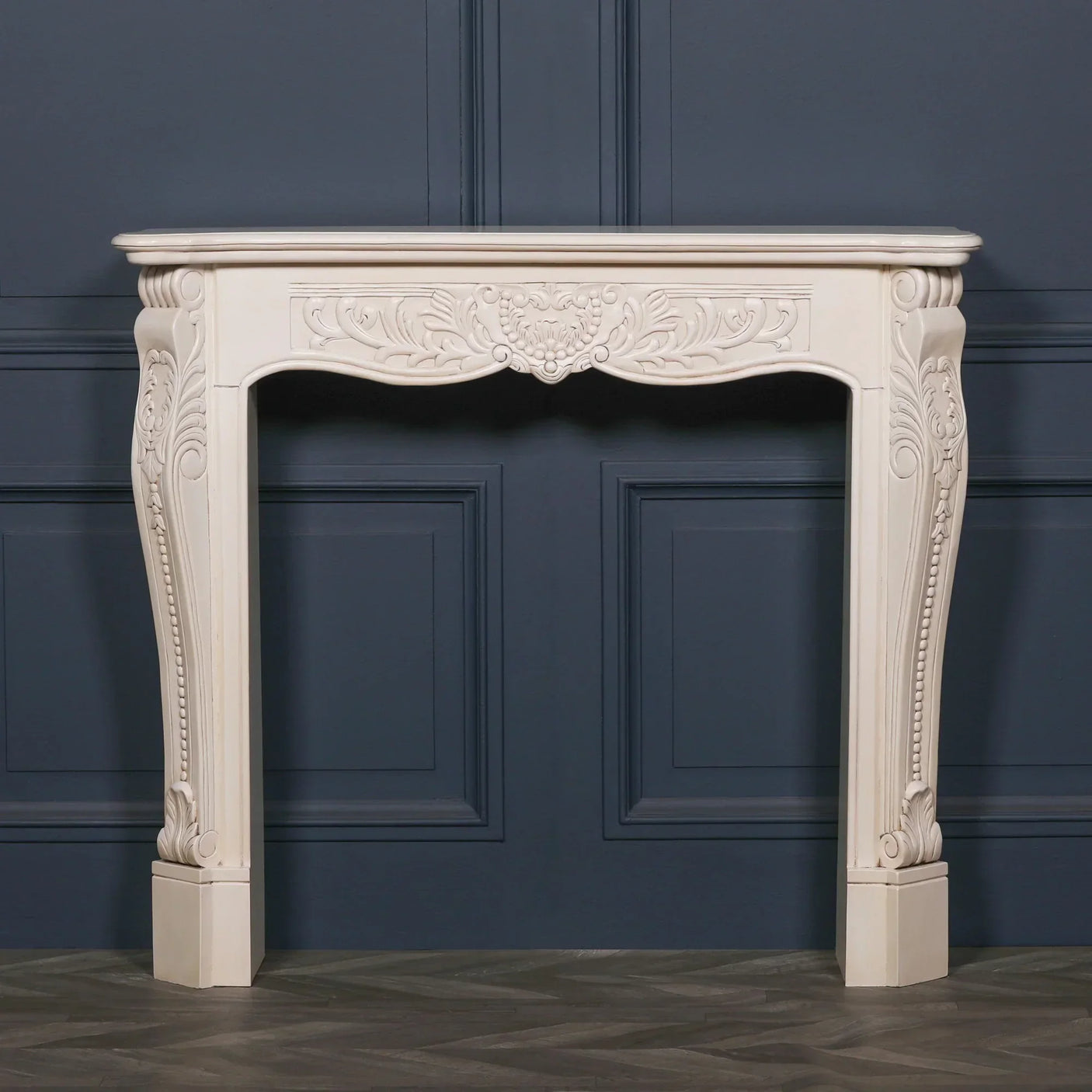 Ivory painted wooden fireplace surround with ornate carved detailing against navy panel wall