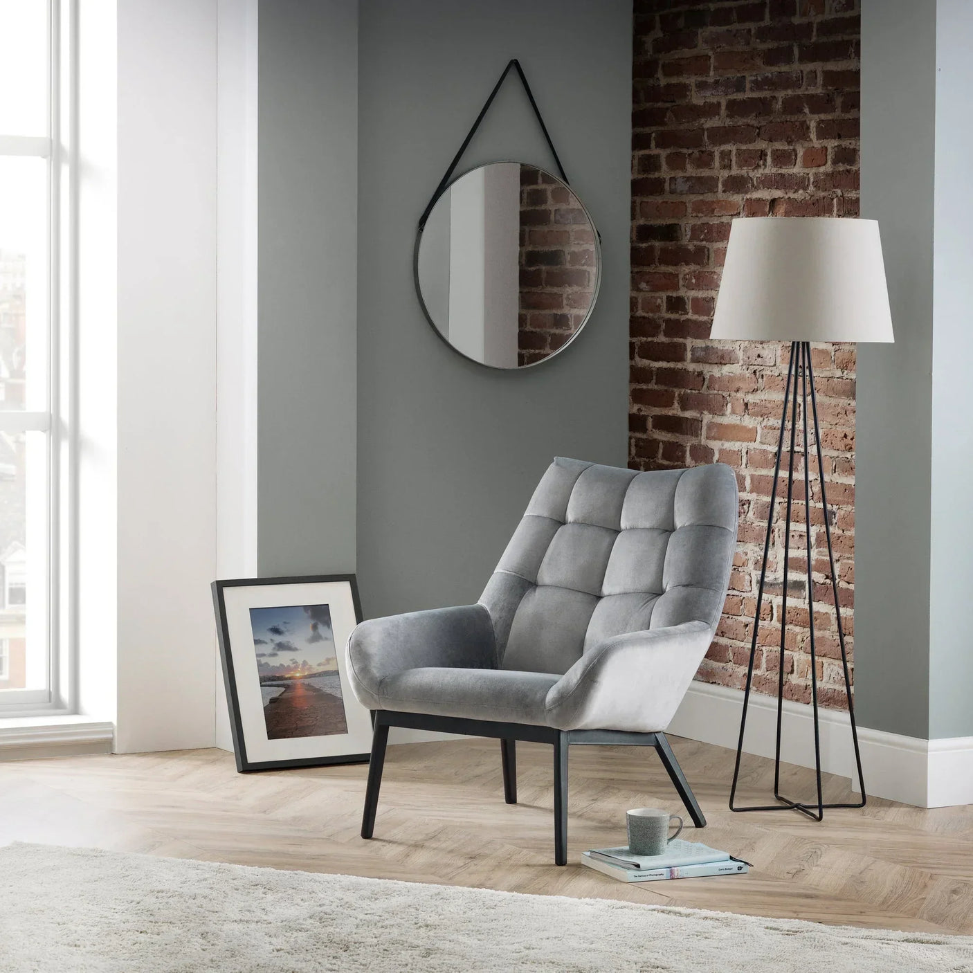 Grey velvet accent chair with black legs in modern living room with brick wall and floor lamp
