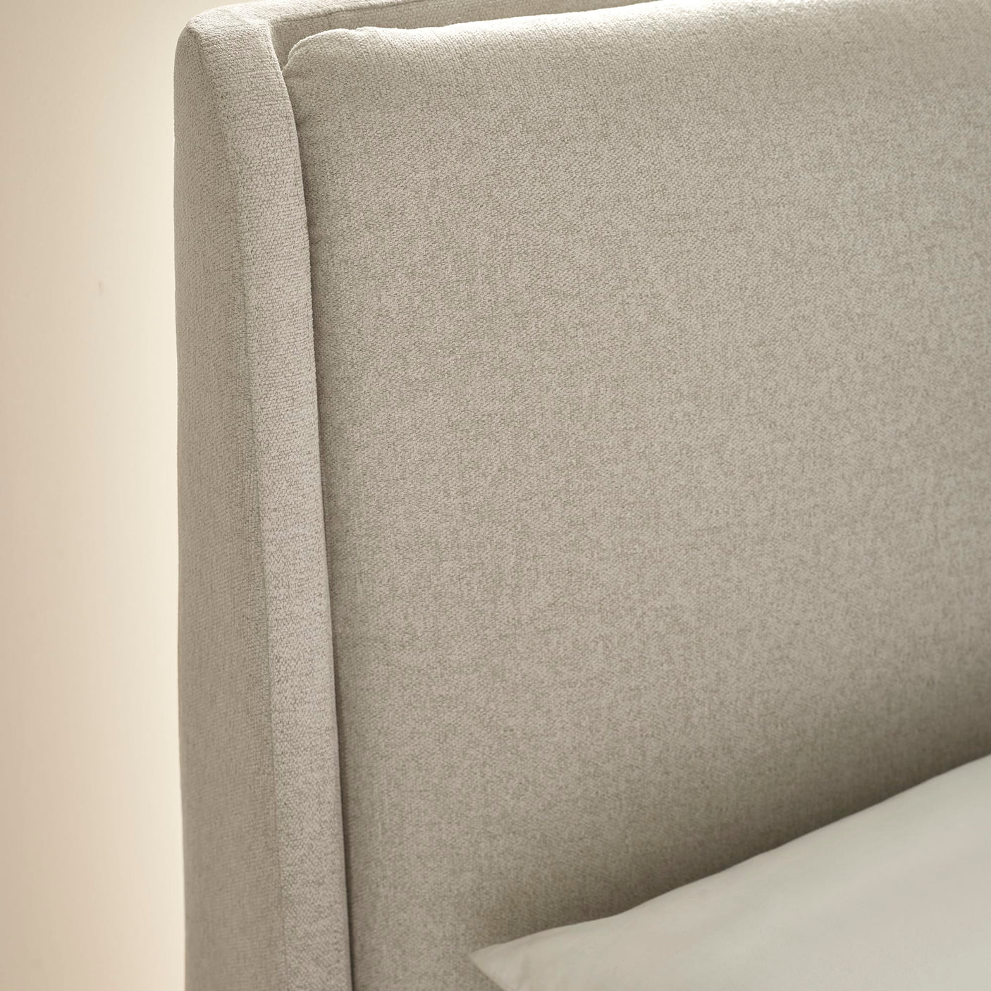 Close-up of beige fabric headboard with seam detail and white pillow