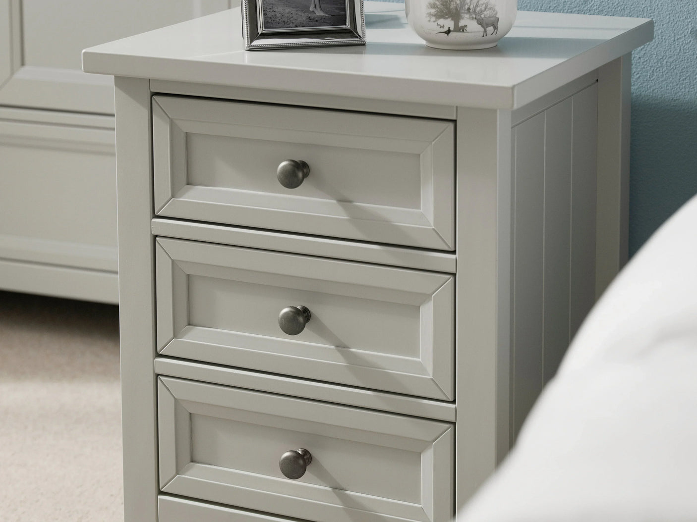Dove grey bedside table with three drawers and metal knobs, close-up view