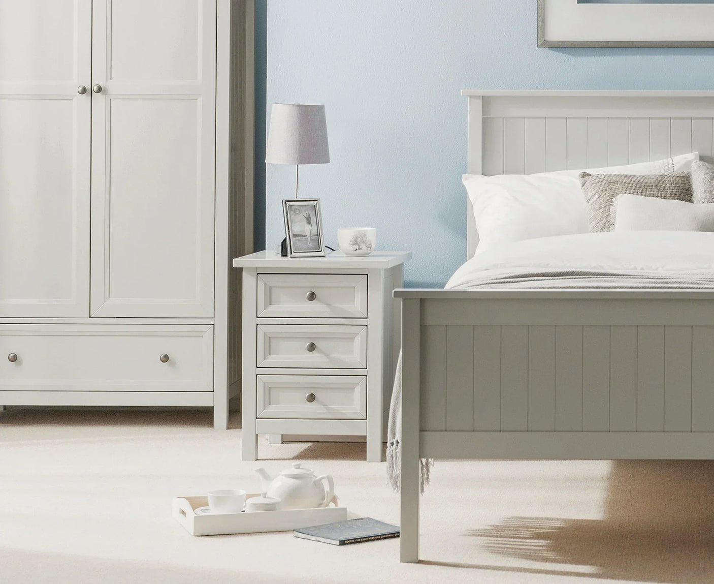 Dove grey 3 drawer bedside table beside matching bed with white bedding in styled bedroom