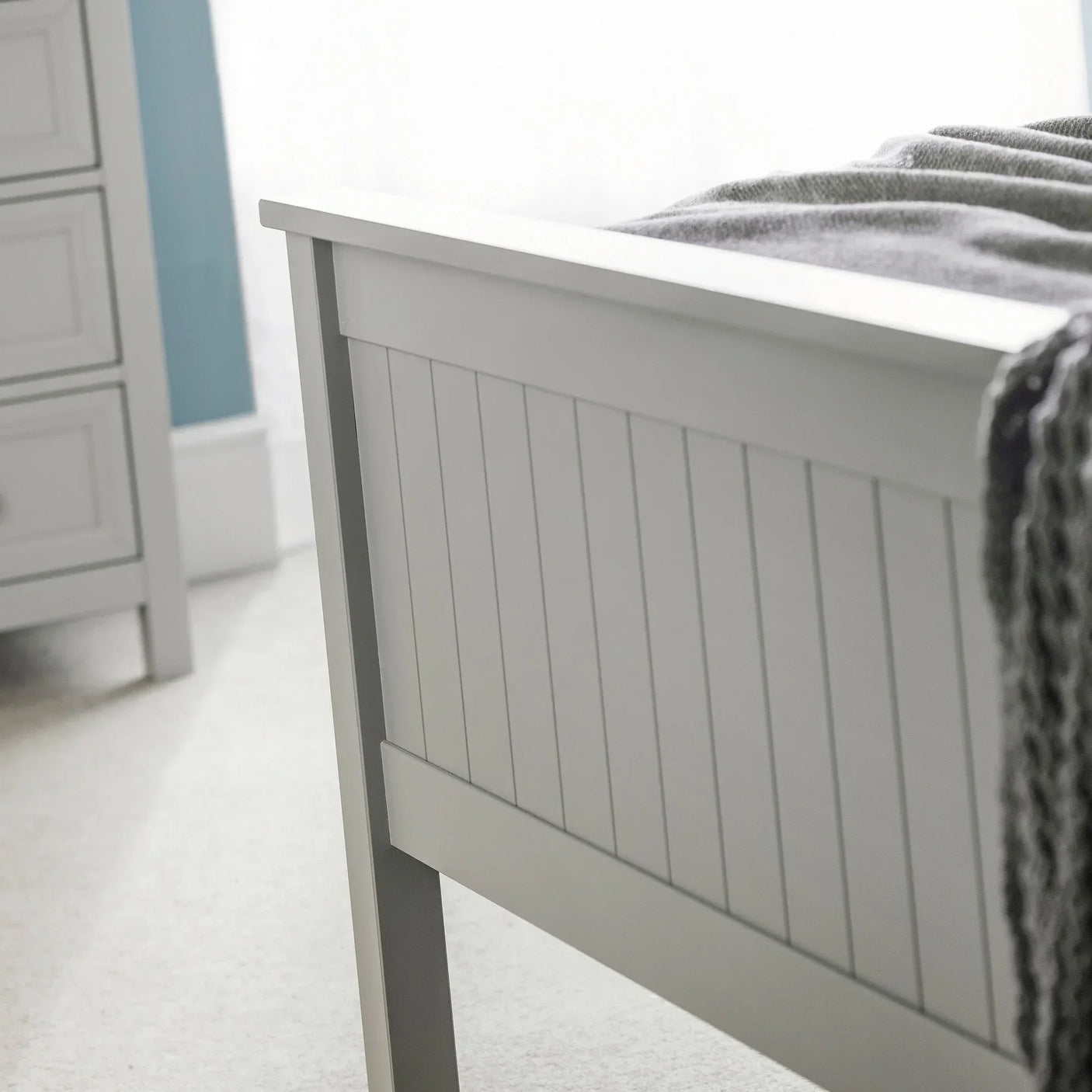 Grey wooden bed footboard with paneled detail in bright bedroom setting