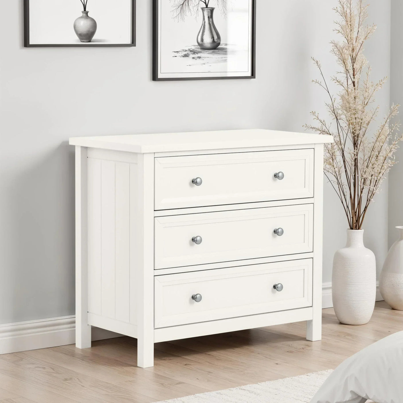 White wooden chest of drawers with three knobs in a modern bedroom setting