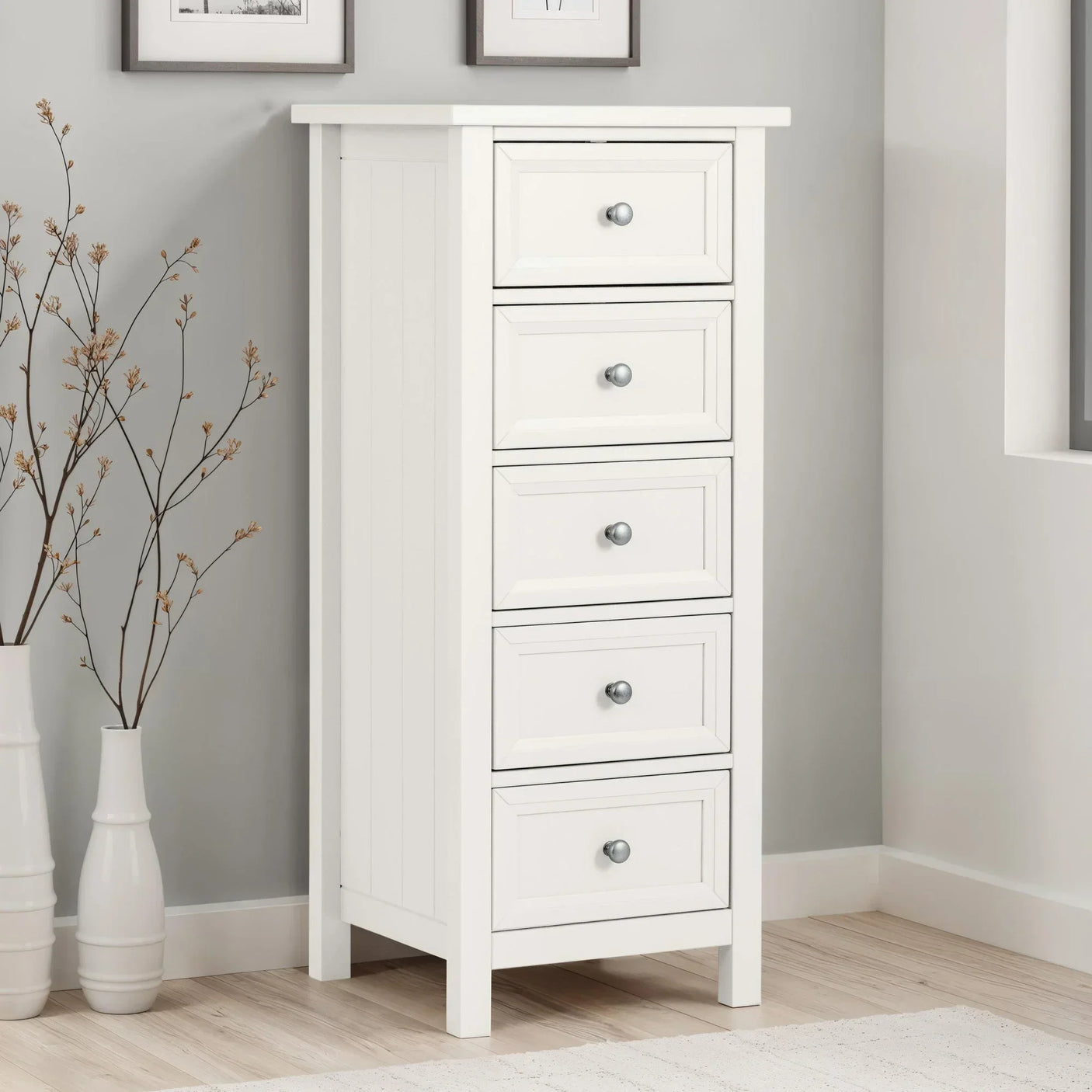 White tall chest of drawers with five drawers and metal handles in a modern bedroom corner