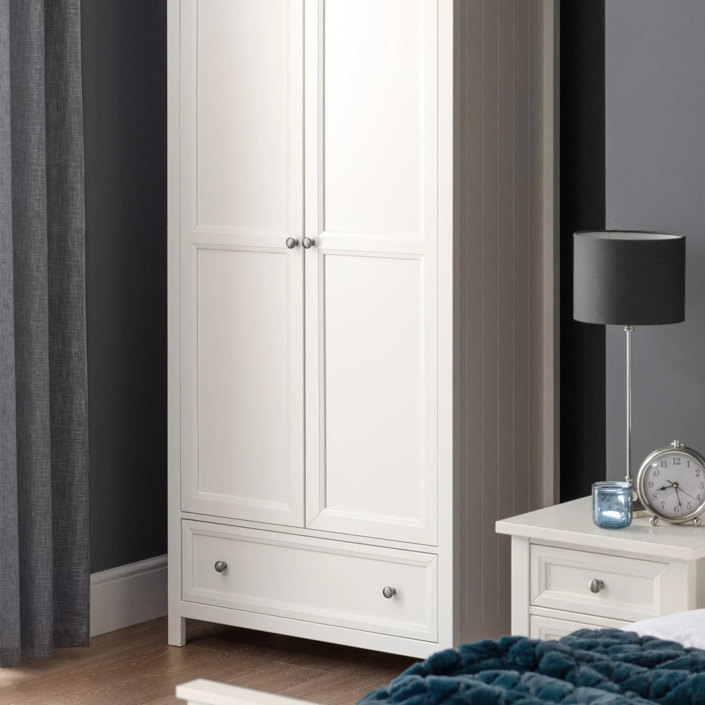 White wooden wardrobe with panel doors and lower drawer in modern bedroom setting