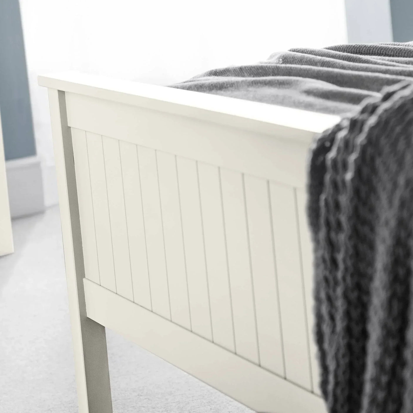 Cream wooden bed frame panel with vertical grooves and grey knit throw blanket draped over