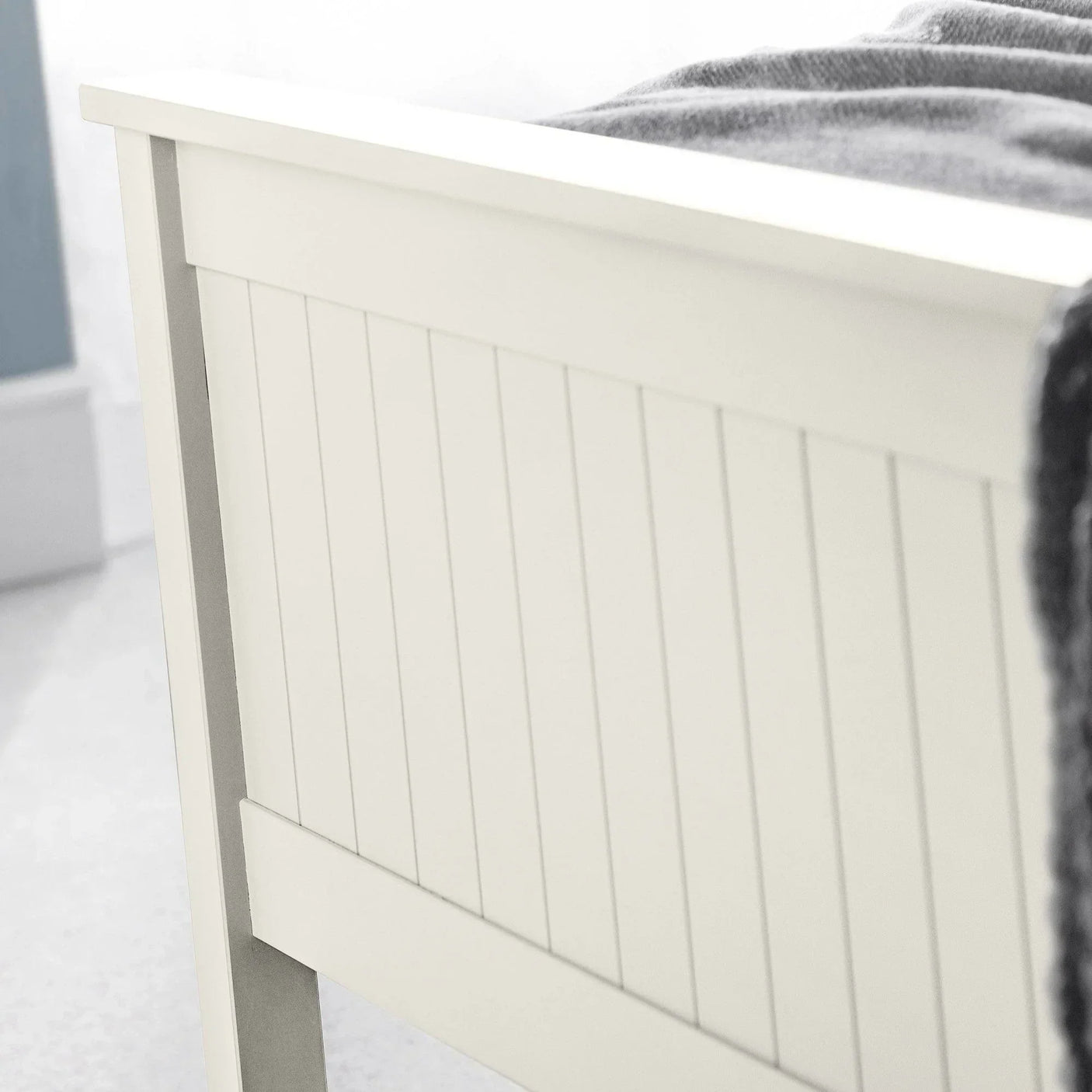 Cream wooden bed footboard with vertical panel detail and soft blanket draped over edge