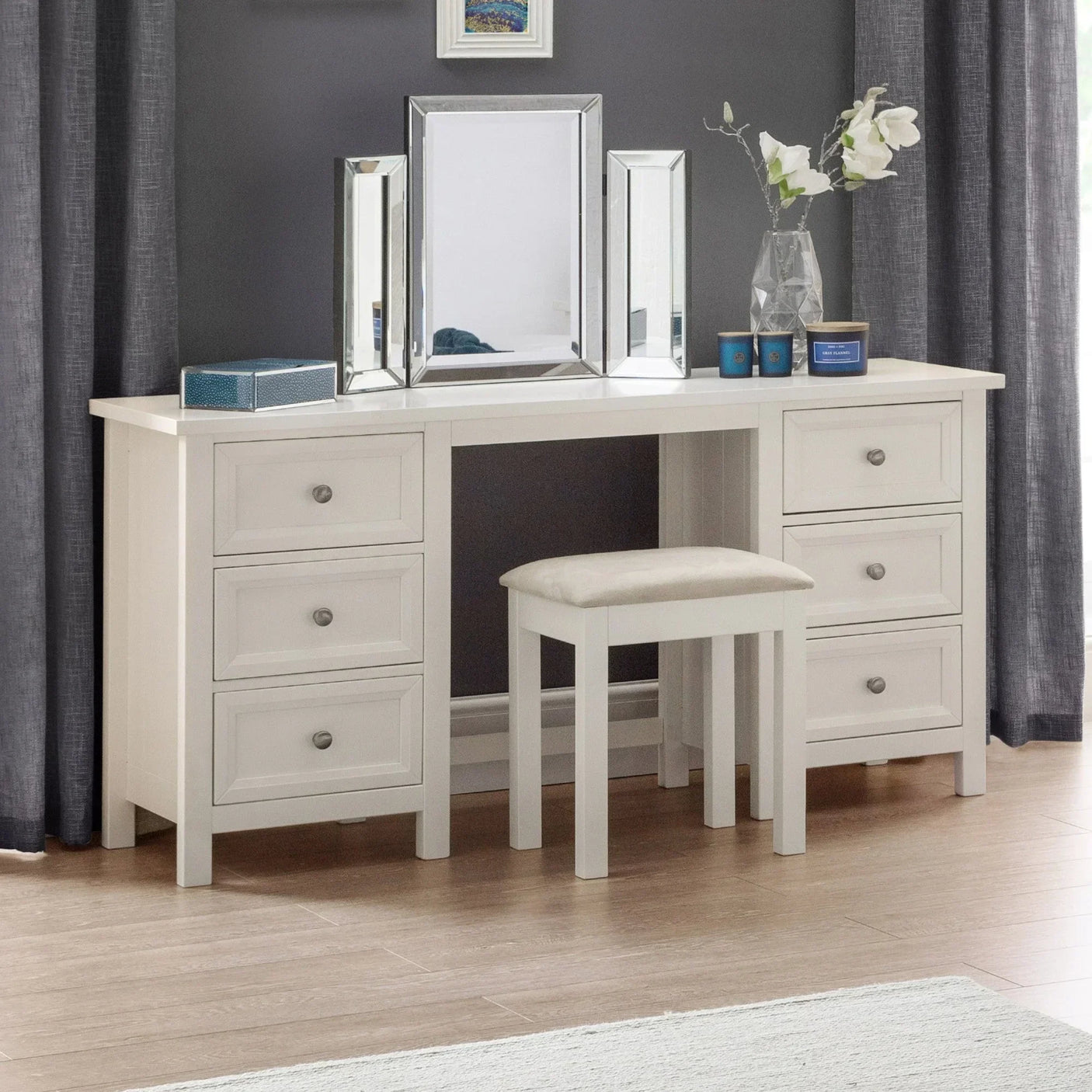 White dressing table with six drawers, matching stool, and trifold mirror in modern bedroom