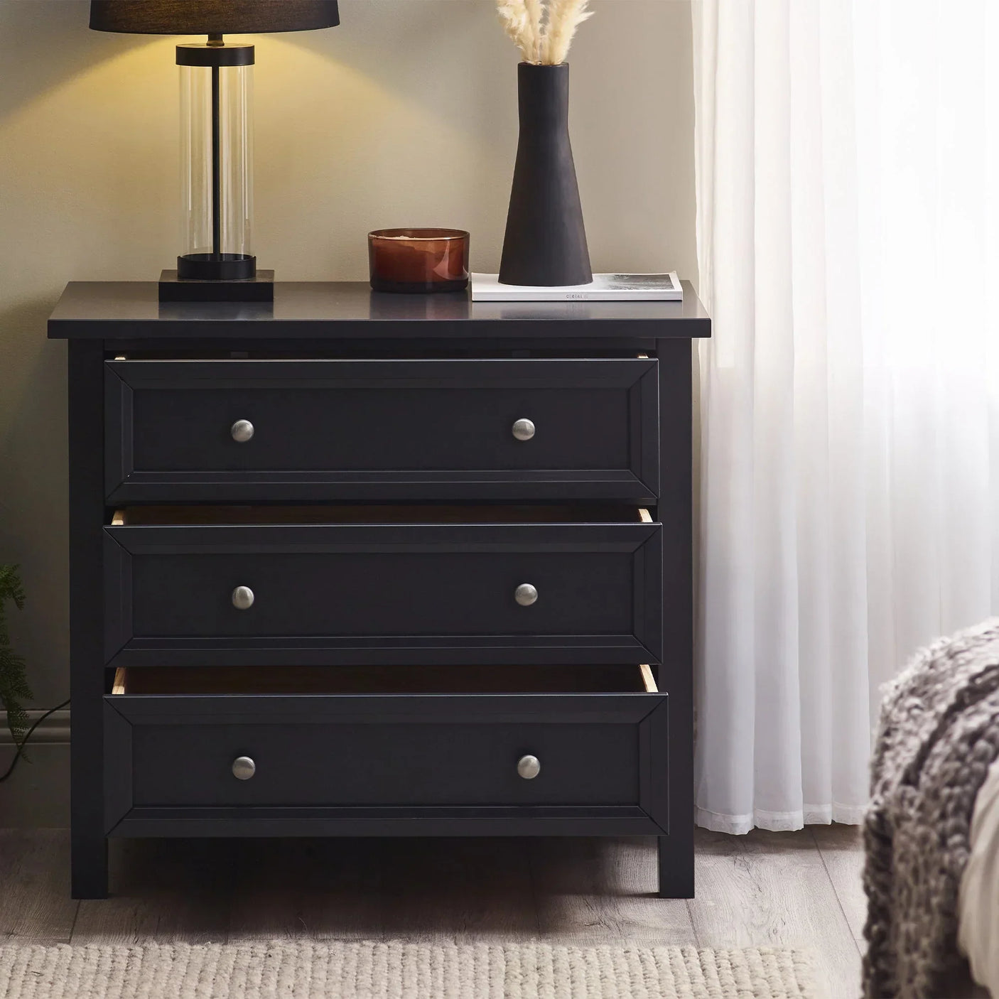 Anthracite three drawer chest with silver knobs in bedroom, lamp and decor on top