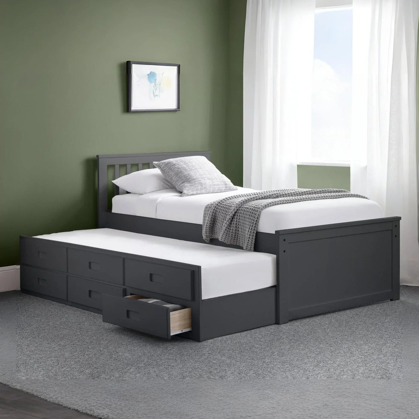 Grey wooden single bed with pull out trundle and storage drawers, set against green wall