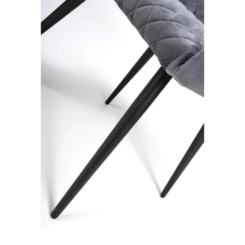 Closeup of grey dining chair with quilted fabric seat and slim black metal legs