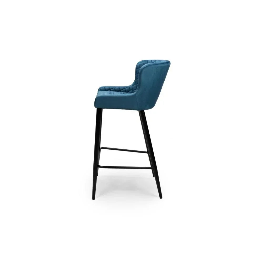 Blue velvet bar stool with quilted backrest and black legs, side profile view