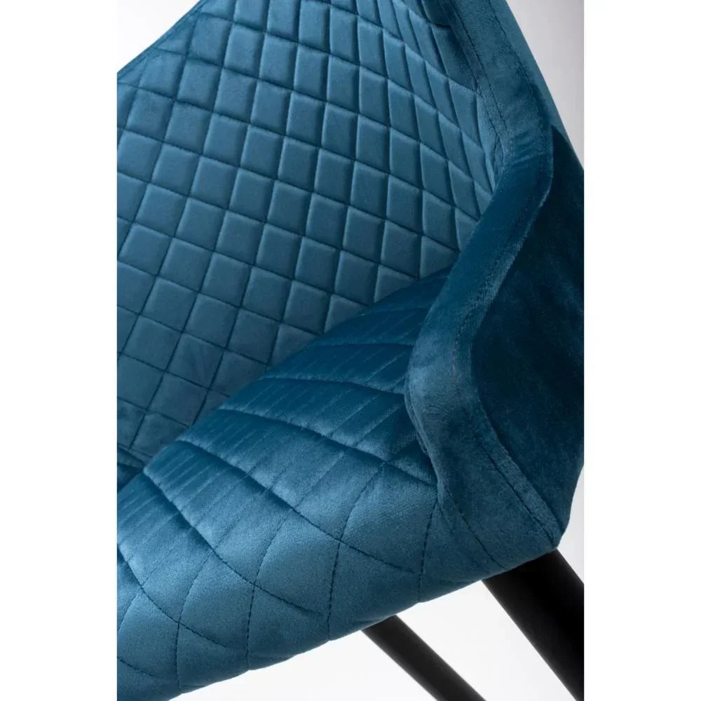 Close up of blue velvet dining chair with diamond quilted stitching and black metal legs