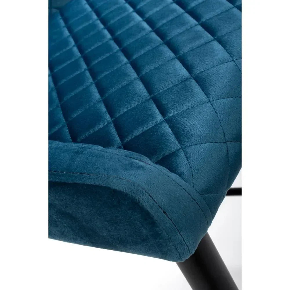Blue velvet dining chair seat with quilted stitching and black metal leg corner view