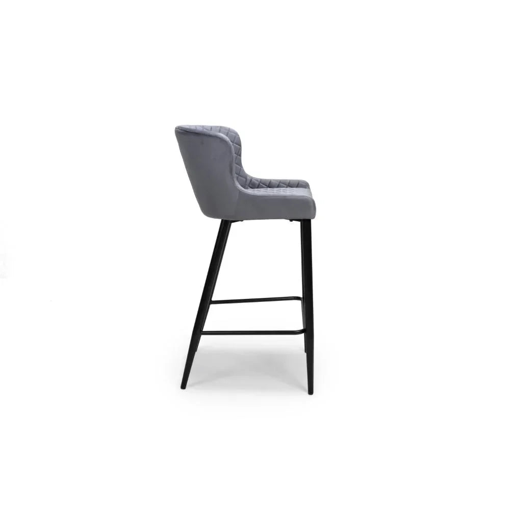 Grey velvet bar stool with quilted backrest and black metal legs, side profile view