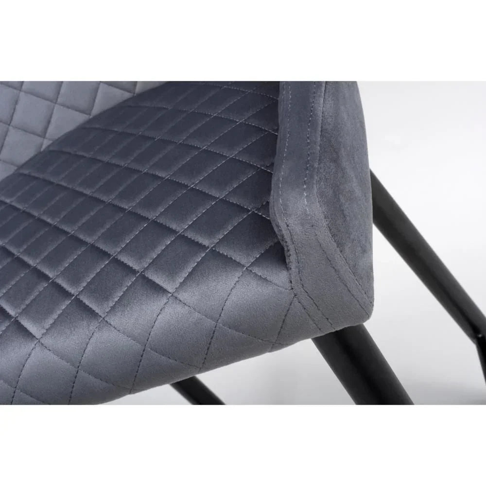 Grey velvet dining chair with quilted seat detail and black metal legs close-up