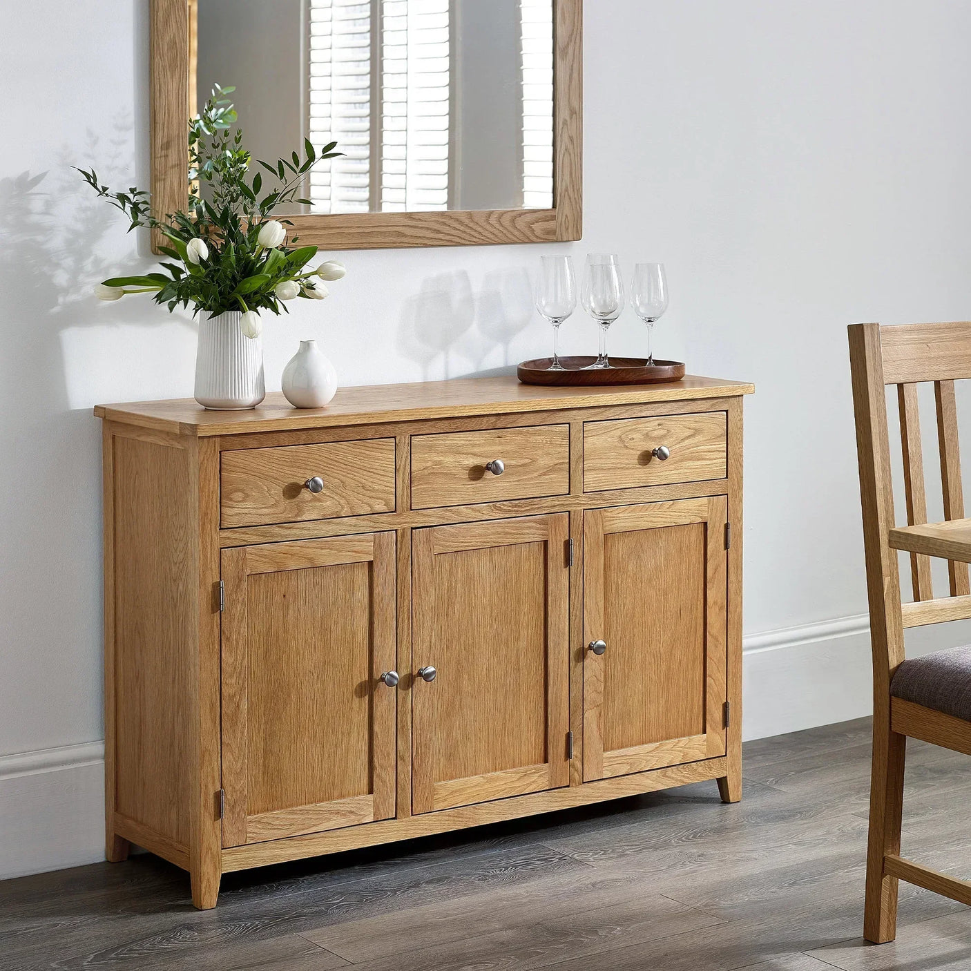 Oak sideboard with three drawers and four doors in dining room, decorated with vases and glasses