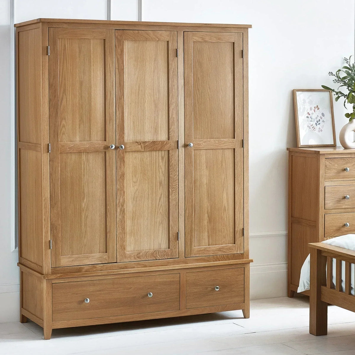 Oak 3 door wardrobe with panelled doors and two drawers in a bright bedroom