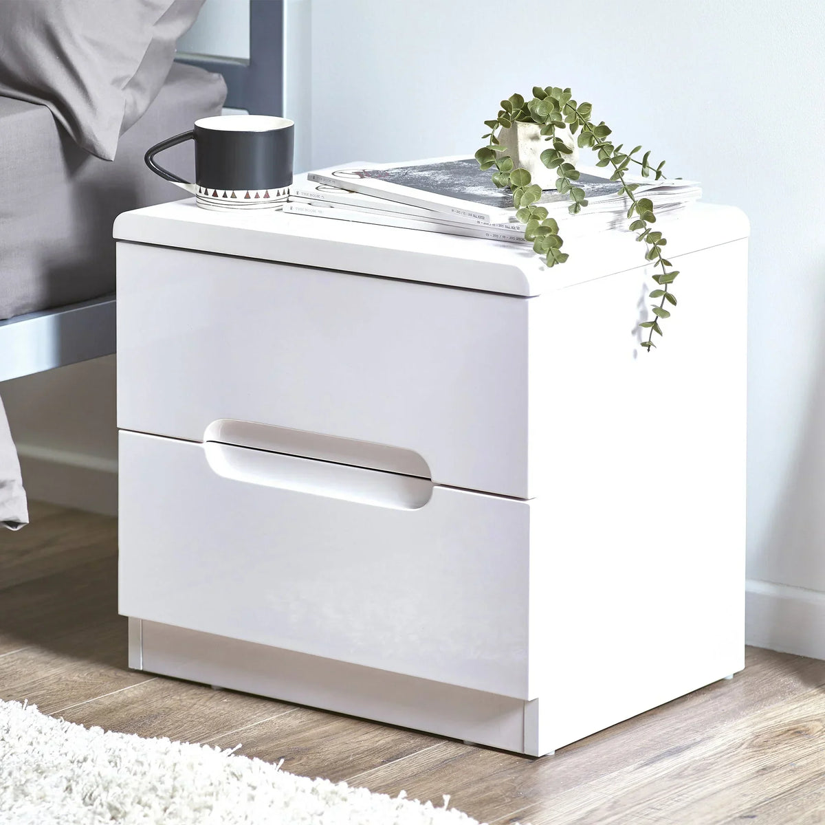 White two drawer bedside table with modern handles, styled with mug and plant beside bed