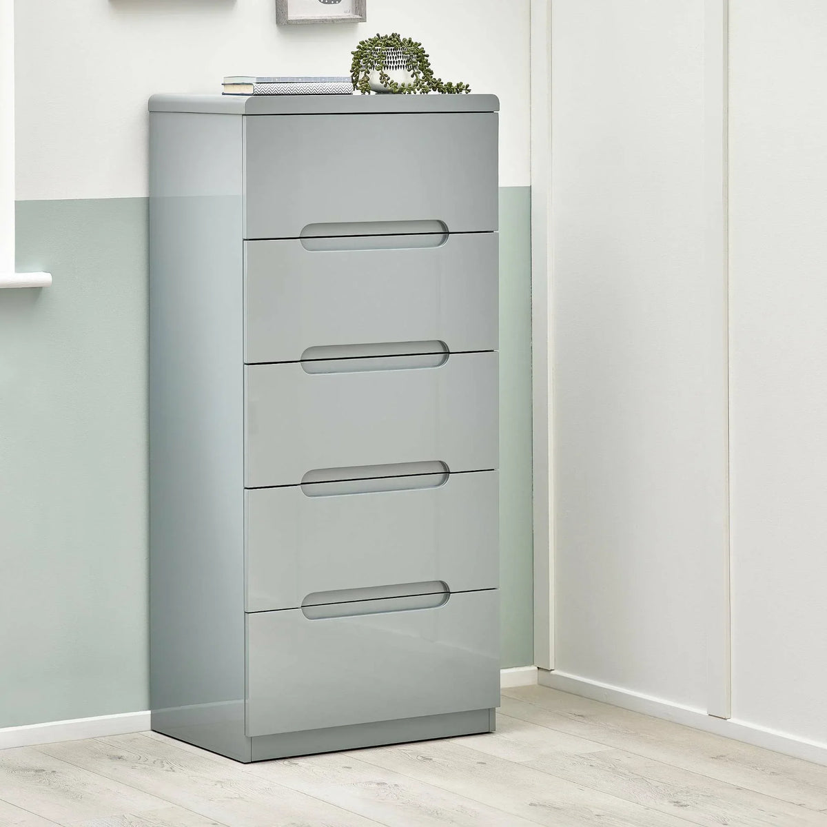Grey five drawer narrow chest with modern handles in a light bedroom corner