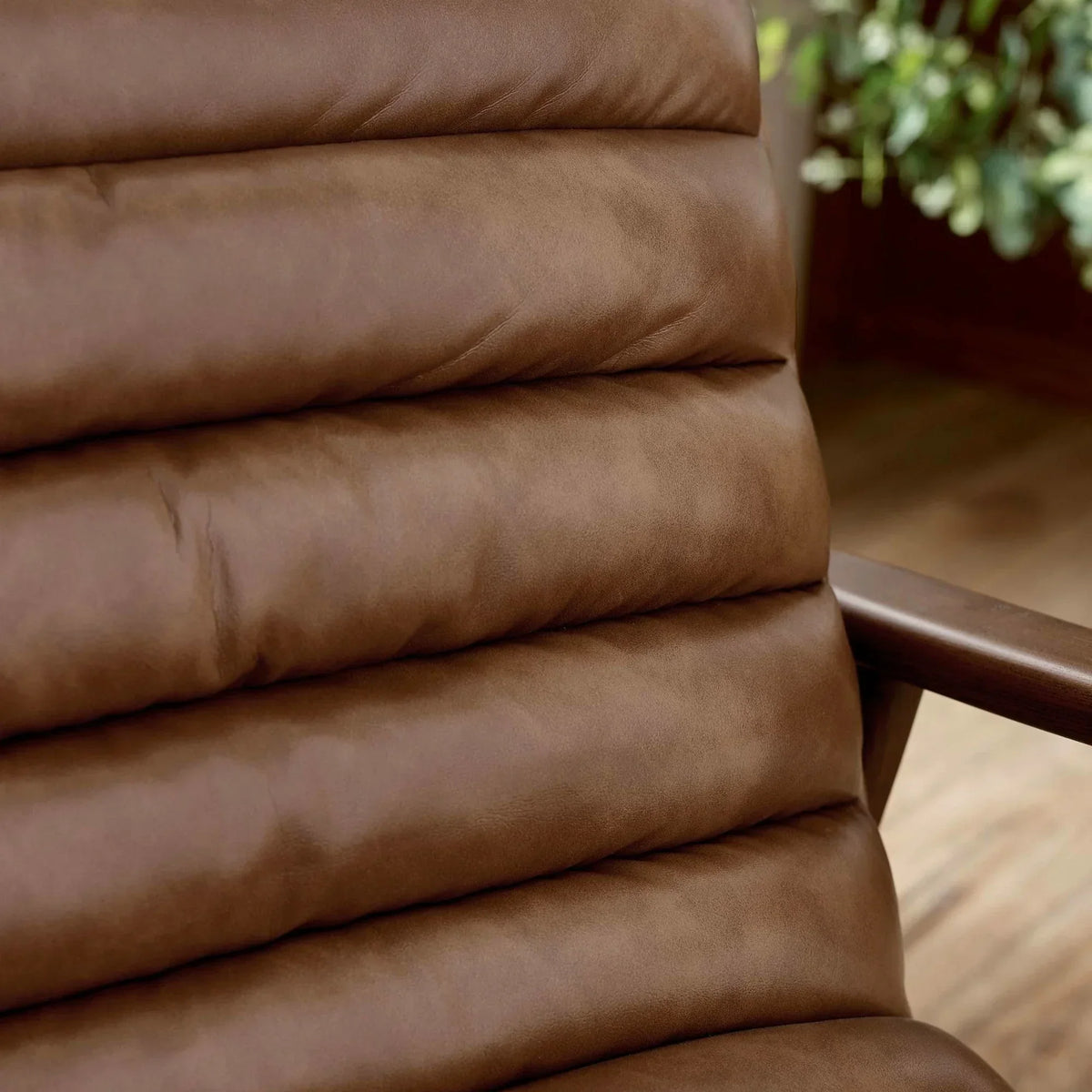 Brown leather armchair with channel-stitched cushion and wooden armrest, close-up view