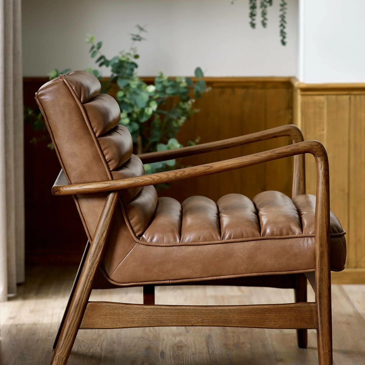 Brown leather armchair with wooden frame and tufted cushions in a modern living room