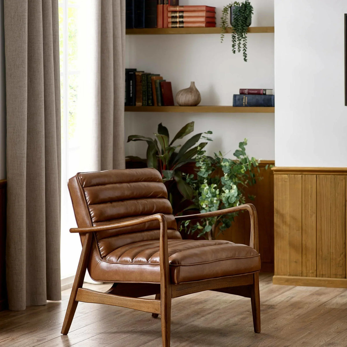 Brown leather accent chair with wooden frame in living room beside bookshelves and plants