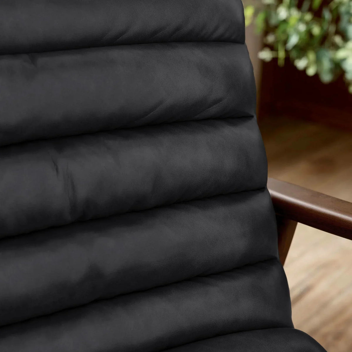 Close-up of black padded chair cushion with wooden armrest and indoor plant in background