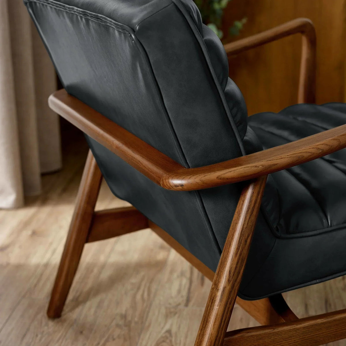 Mid-century armchair with black leather seat and wooden frame on wood flooring