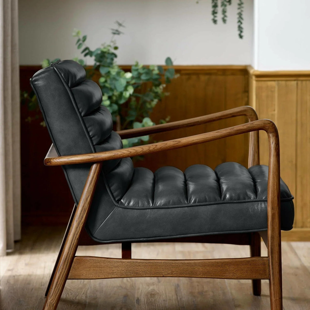 Black leather accent chair with tufted cushions and oak wood frame, side view