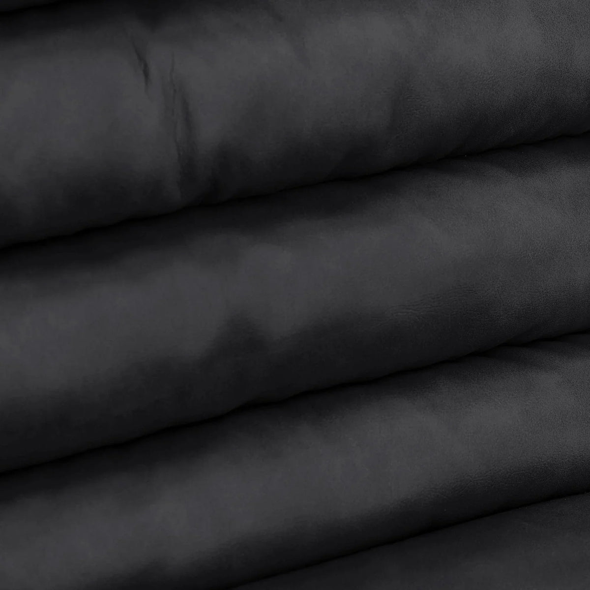 Closeup of black faux leather upholstery fabric with smooth texture and folded layers