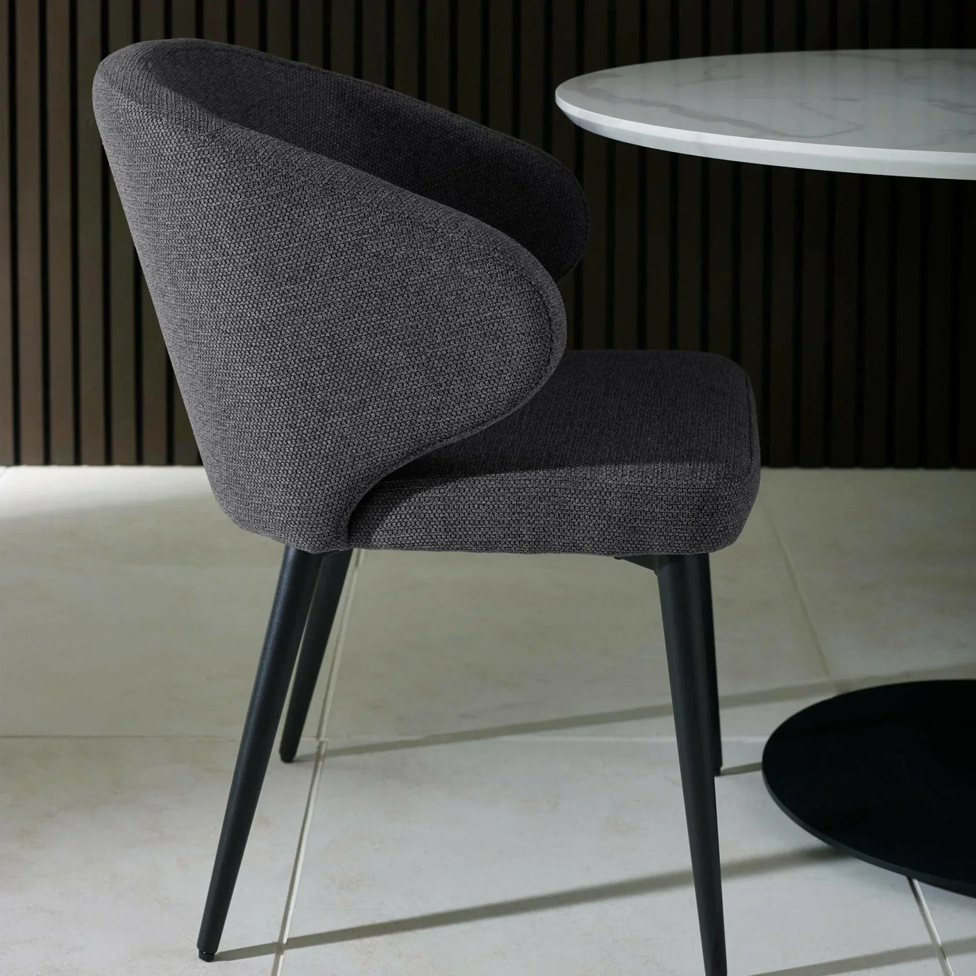 Dark grey fabric dining chair with curved backrest and black metal legs beside a marble table