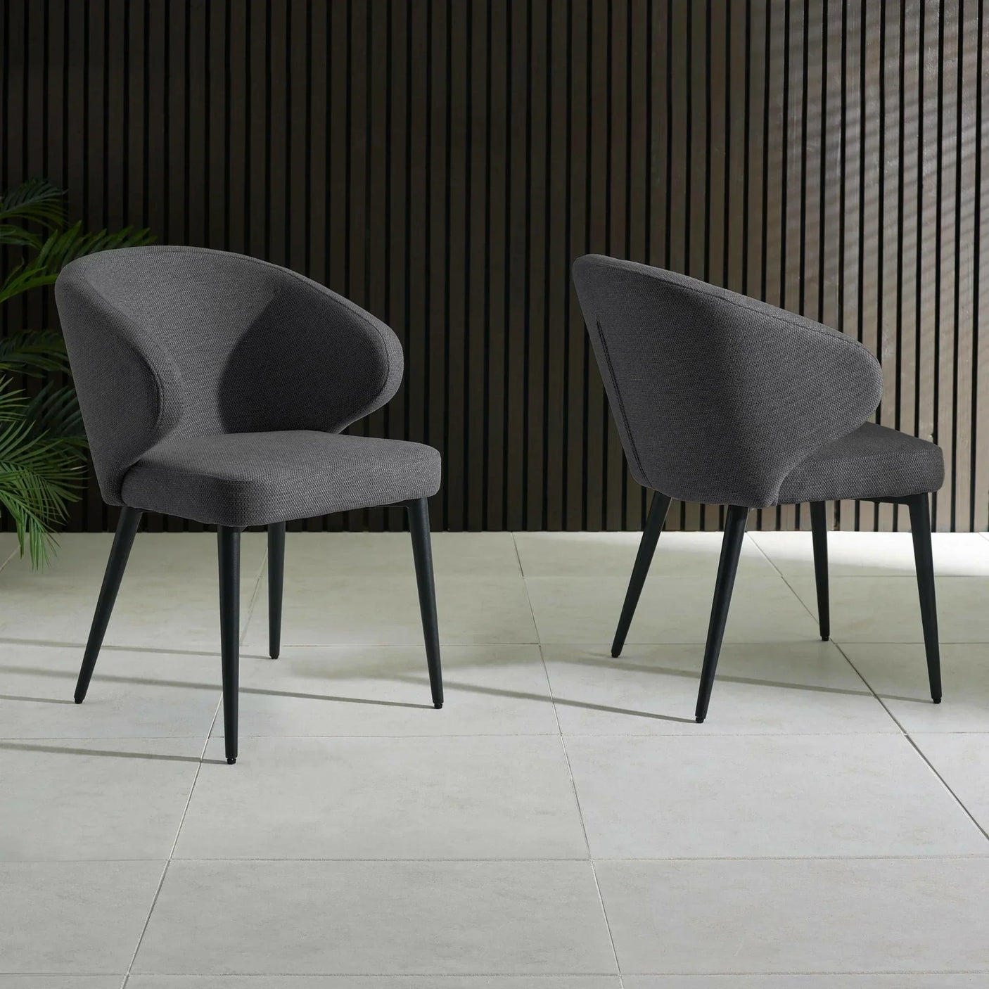 Pair of dark grey fabric dining chairs with curved backs on tiled floor