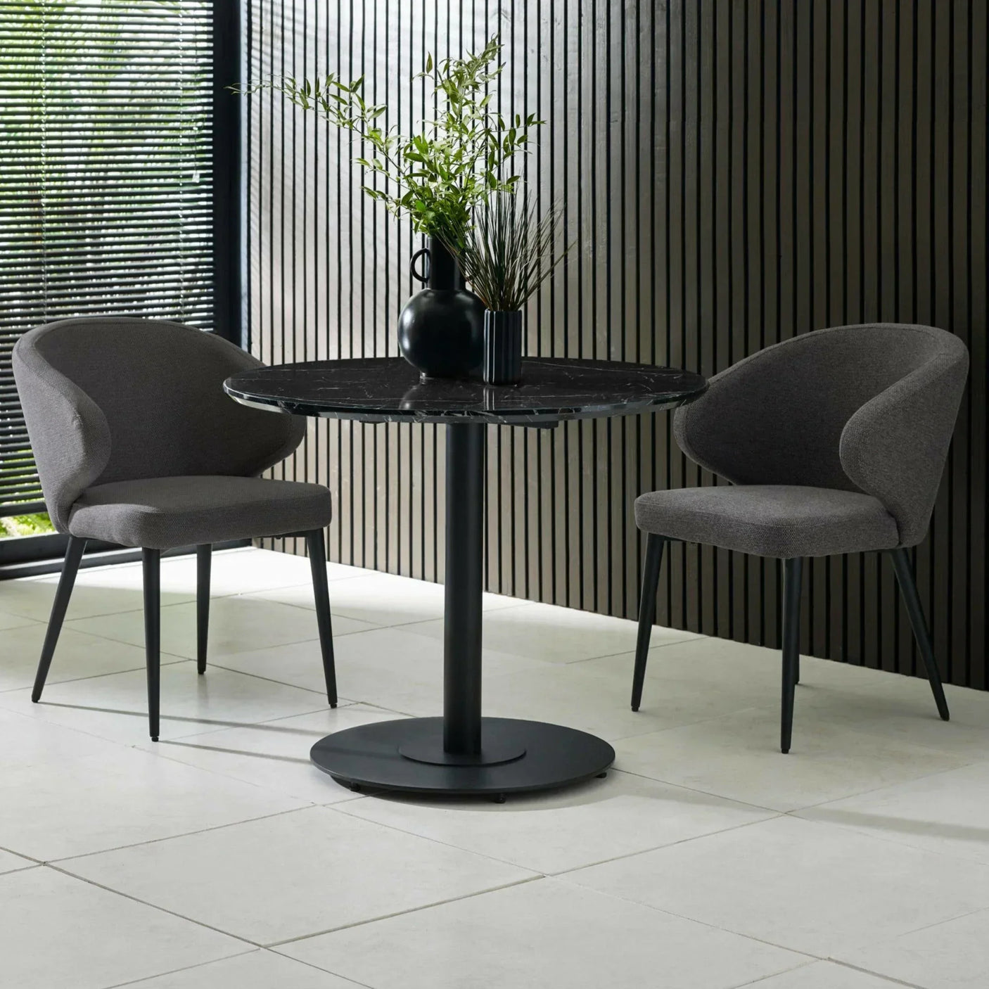 Black round dining table with marble top and two grey upholstered dining chairs