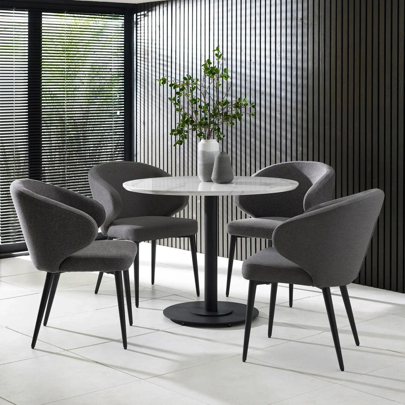 Modern round dining table with white top and four grey fabric chairs in bright room